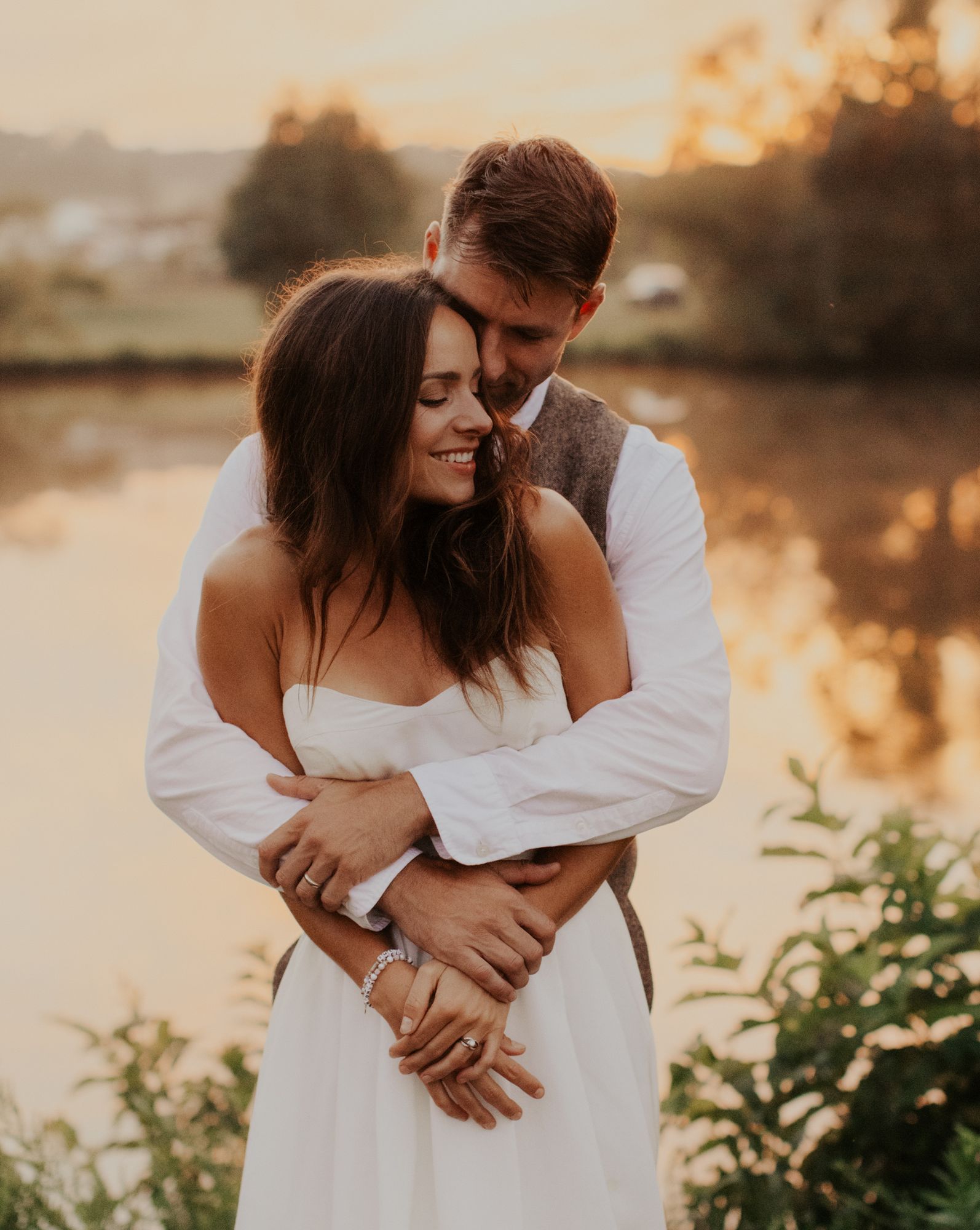 Groom embracing the bride from behind at sunset