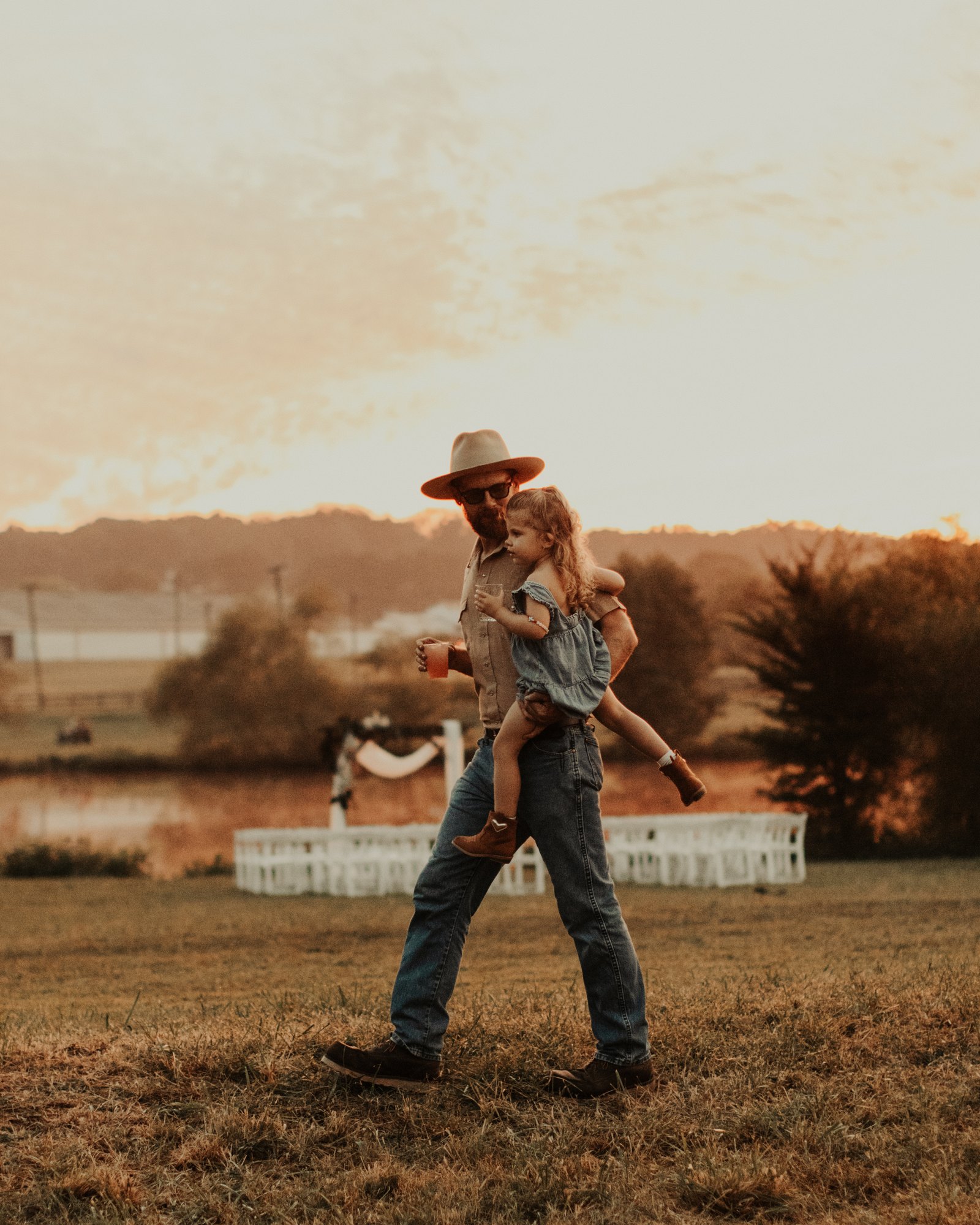A guest carries his daughter across the field at sunset