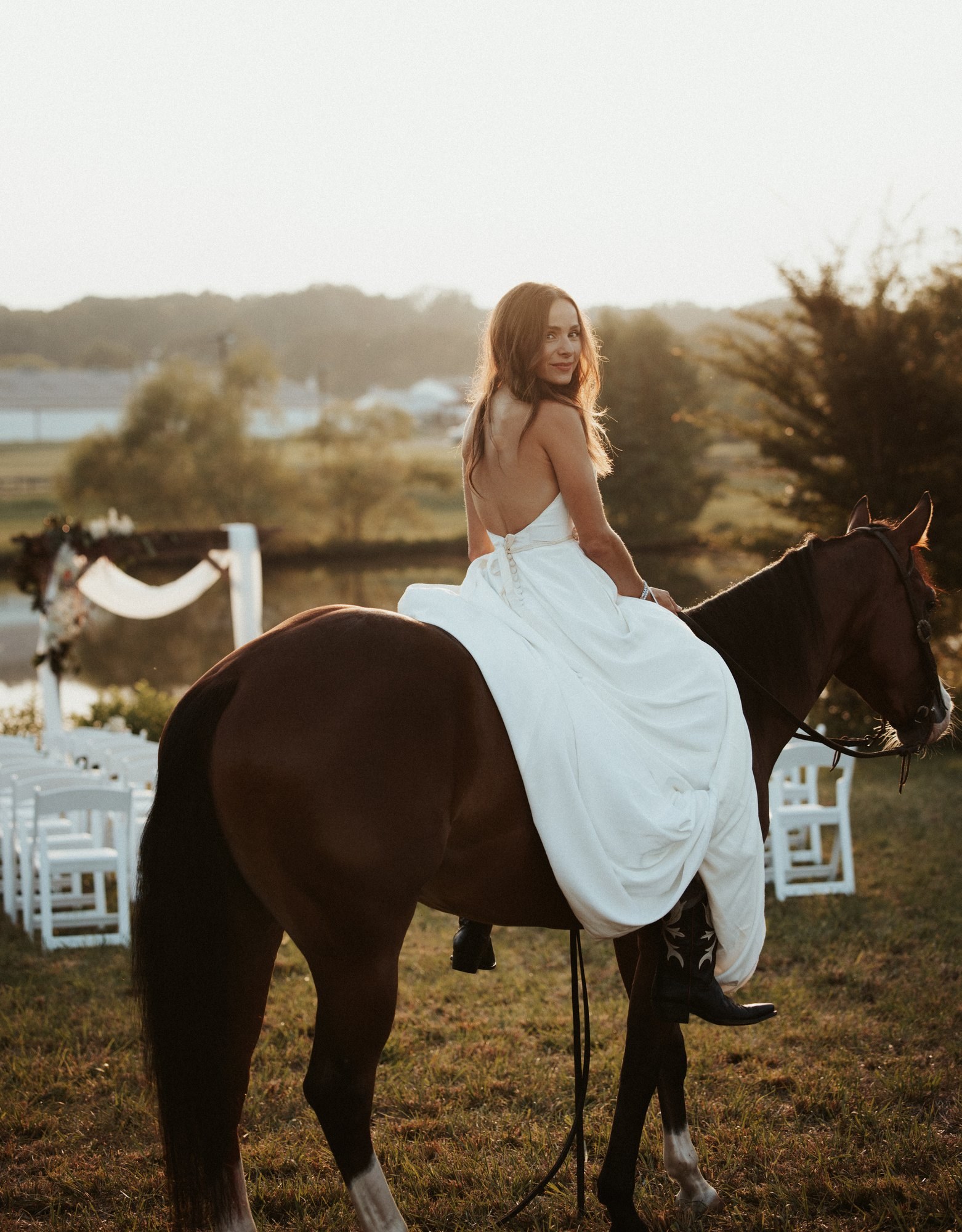 Bride on horseback beside the pond, with the ceremony chairs behind her