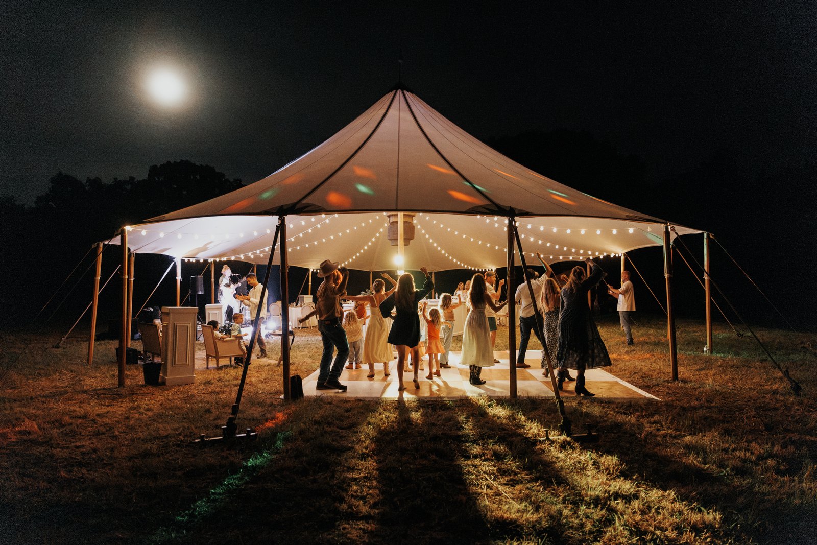 Guests dancing under the lit sailcloth tent beneath a full moon